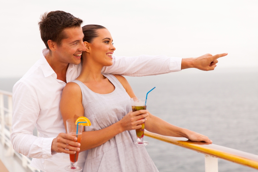 cheerful couple with cocktails enjoying sea view from cruise ship