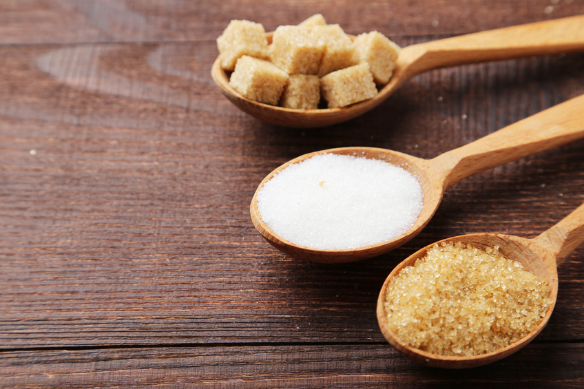 Various kinds of sugar in spoons on brown wooden background