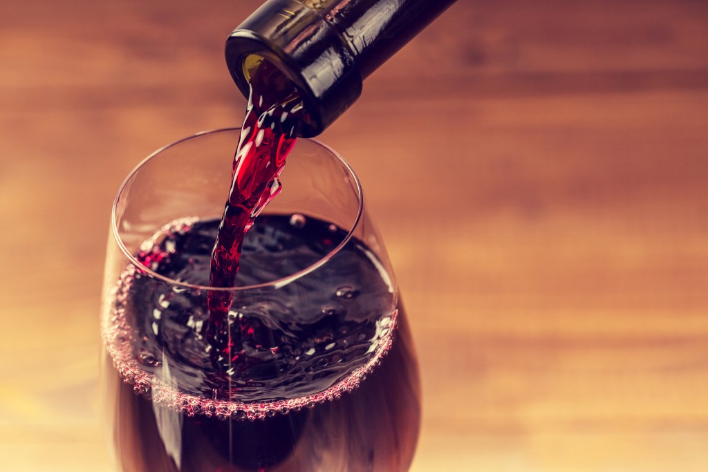 Pouring red wine into the glass against wooden background