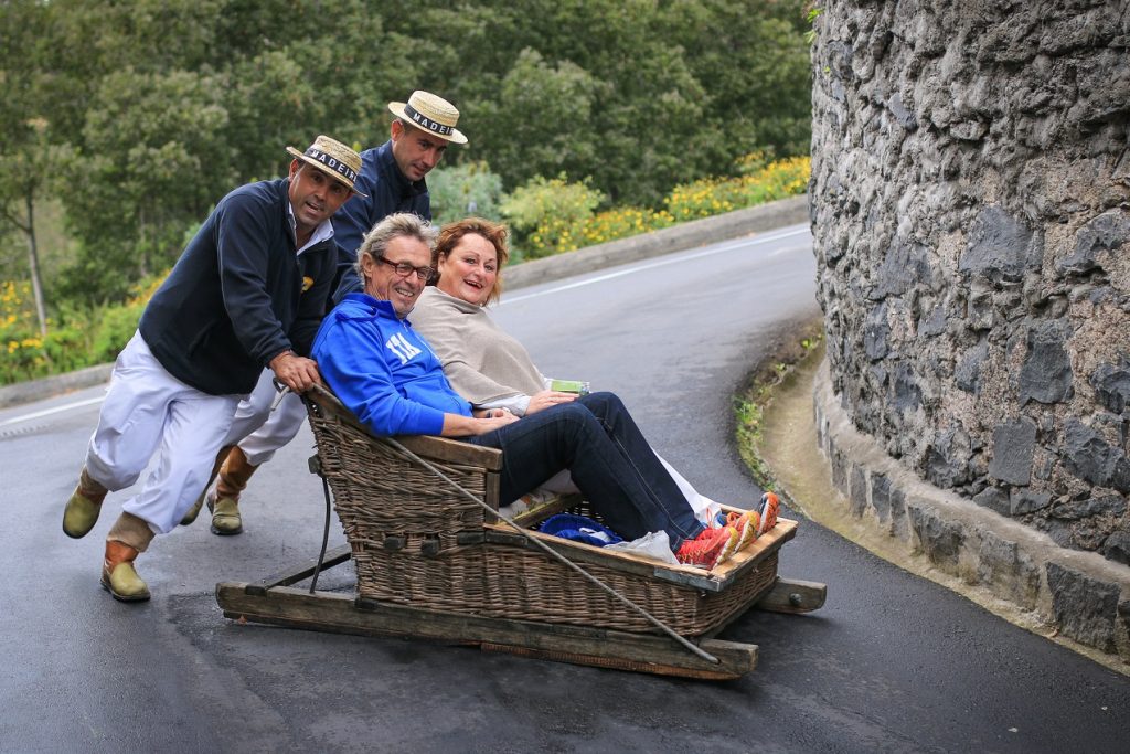 Funchal, Portugal - November 11, 2015: Tourists enjoying a ride on toboggan (traditional sled) through the streets of Madeira's capital city.